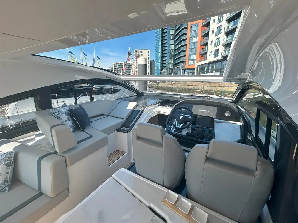Luxurious yacht interior with modern seating, Garmin dashboard, and panoramic views of city buildings and flags.